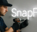 Monter instaluje neonowy napis SnapFix na szarej ścianie za pomocą wkrętarki.