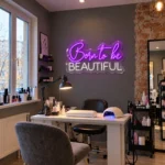 Neon Born to be BEAUTIFUL LED – fioletowy i biały napis nad stanowiskiem manicure